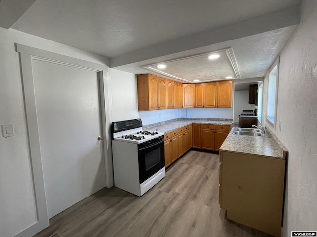 kitchen with sink, a textured ceiling, wood-type flooring, and white range with gas stovetop