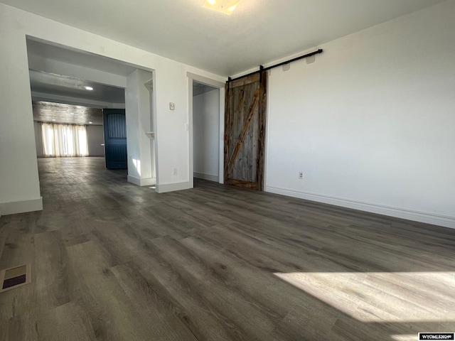 empty room with a barn door and dark wood-type flooring