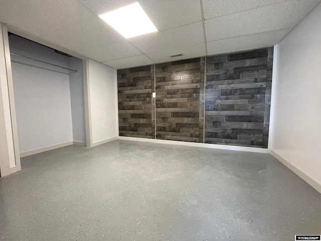 basement featuring a drop ceiling and wooden walls