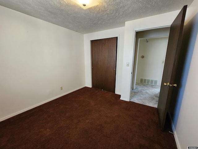 unfurnished bedroom with dark carpet, a closet, and a textured ceiling