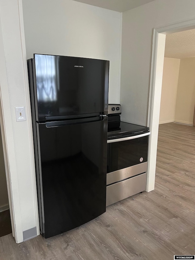 kitchen with stainless steel electric range oven, a textured ceiling, light wood-type flooring, and black refrigerator