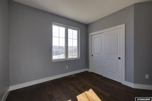 unfurnished bedroom with baseboards, dark wood-type flooring, and a closet