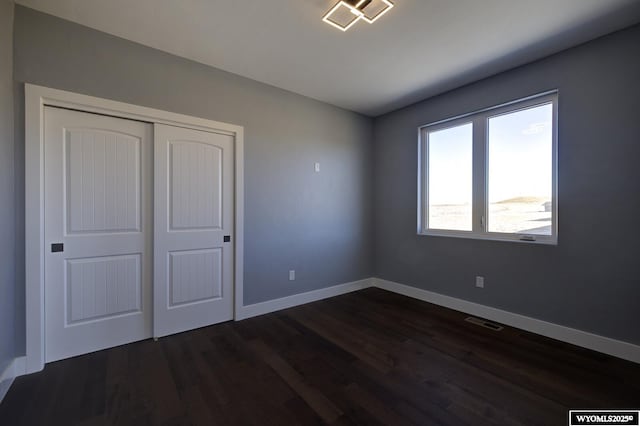 unfurnished bedroom with dark wood-type flooring, baseboards, and a closet