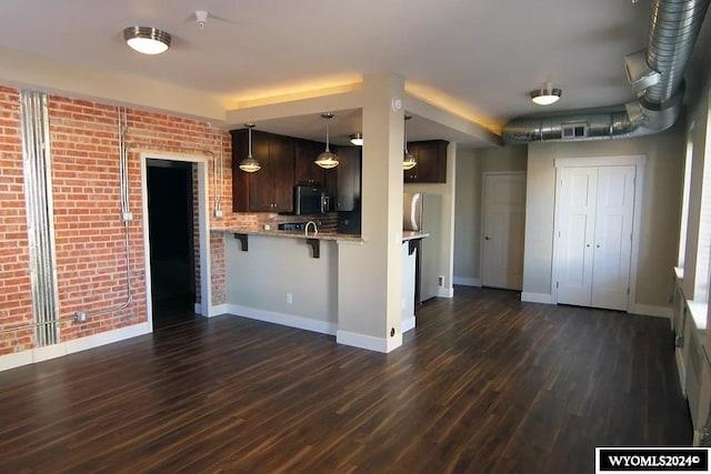 kitchen featuring dark brown cabinets, dark hardwood / wood-style flooring, kitchen peninsula, brick wall, and a breakfast bar