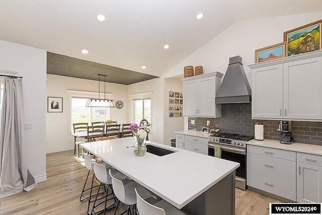 kitchen featuring gas range, light hardwood / wood-style flooring, an island with sink, vaulted ceiling, and custom exhaust hood