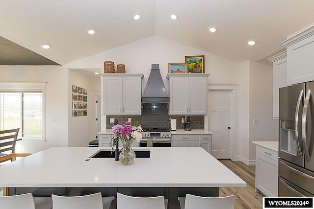 kitchen with appliances with stainless steel finishes, premium range hood, an island with sink, and vaulted ceiling