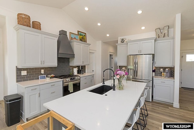 kitchen with custom exhaust hood, backsplash, vaulted ceiling, light hardwood / wood-style floors, and stainless steel appliances