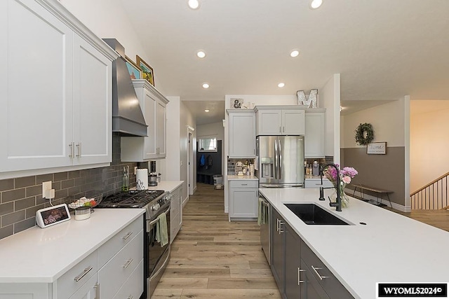 kitchen with wall chimney range hood, appliances with stainless steel finishes, sink, backsplash, and light hardwood / wood-style floors