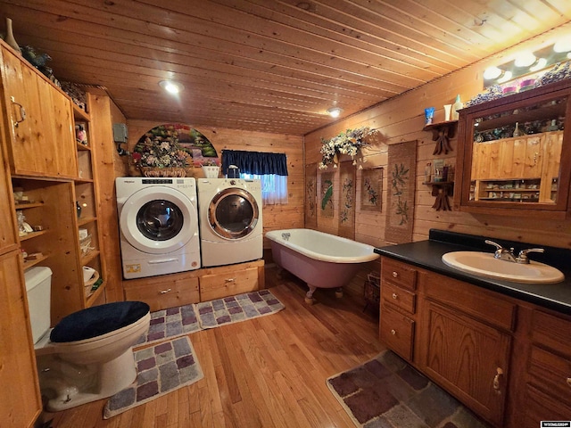 bathroom featuring hardwood / wood-style floors, washer and dryer, toilet, a bath, and wooden walls