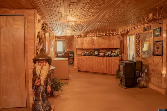 interior space featuring a wood stove, wooden walls, light brown cabinetry, and wood ceiling