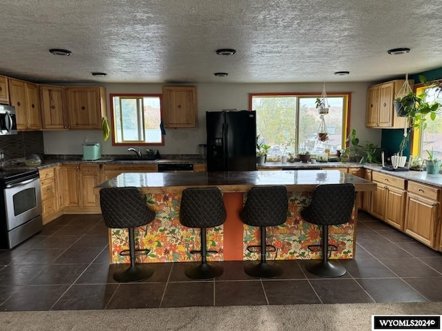 kitchen featuring dark tile patterned flooring, black appliances, sink, a kitchen bar, and a kitchen island