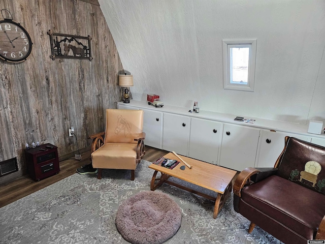 sitting room with dark wood-type flooring, wooden walls, and vaulted ceiling