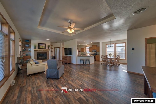 living room featuring a textured ceiling, dark wood-type flooring, a raised ceiling, and ceiling fan