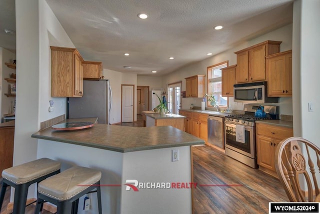 kitchen with a kitchen breakfast bar, kitchen peninsula, stainless steel appliances, a textured ceiling, and dark hardwood / wood-style flooring