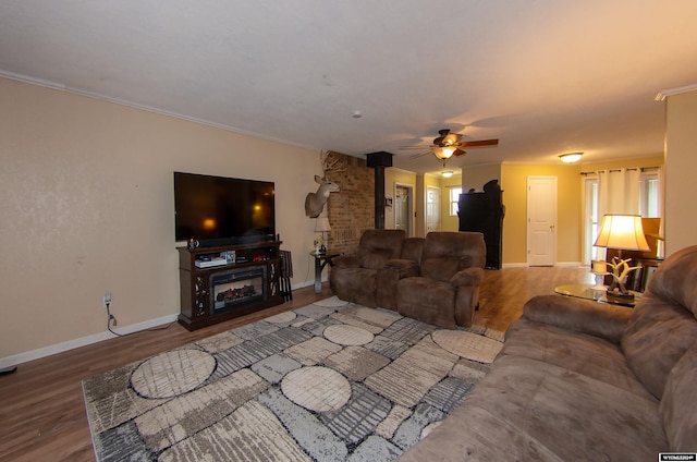 living room featuring a wood stove, ceiling fan, wood-type flooring, and crown molding