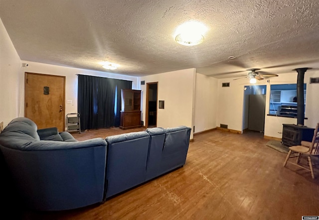 living room featuring wood-type flooring, a textured ceiling, a wood stove, and ceiling fan