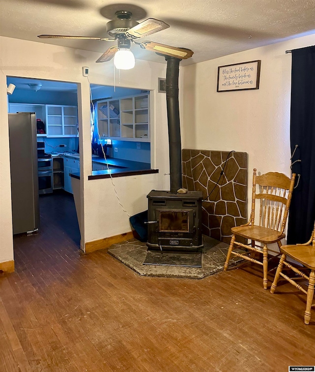 living room featuring a textured ceiling, wood-type flooring, a wood stove, and ceiling fan