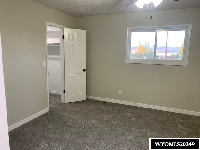 unfurnished bedroom featuring dark colored carpet, ceiling fan, a spacious closet, a textured ceiling, and a closet