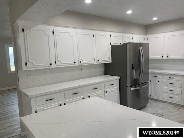 kitchen with light stone countertops, stainless steel refrigerator with ice dispenser, and white cabinetry