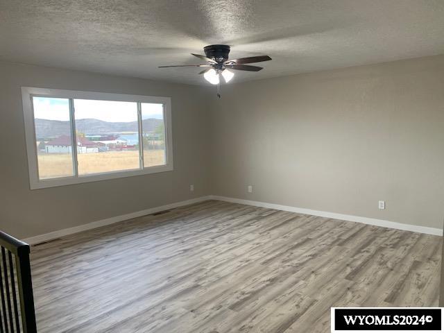 unfurnished room featuring a mountain view, a textured ceiling, light hardwood / wood-style flooring, and ceiling fan