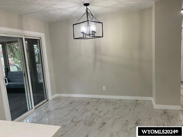 unfurnished dining area featuring a textured ceiling and a chandelier