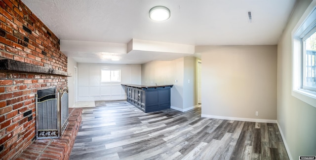 unfurnished living room with a textured ceiling, a brick fireplace, a wealth of natural light, and dark wood-type flooring