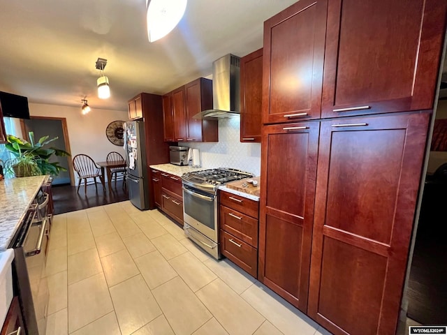 kitchen with decorative backsplash, hanging light fixtures, appliances with stainless steel finishes, wall chimney exhaust hood, and light stone counters