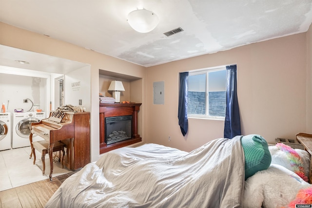 bedroom featuring electric panel, washer and clothes dryer, and light hardwood / wood-style flooring