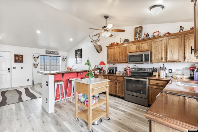 kitchen with lofted ceiling, a kitchen breakfast bar, appliances with stainless steel finishes, and light hardwood / wood-style floors