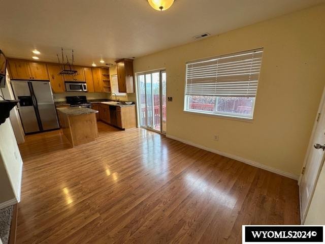 kitchen with a kitchen island, sink, pendant lighting, light wood-type flooring, and appliances with stainless steel finishes