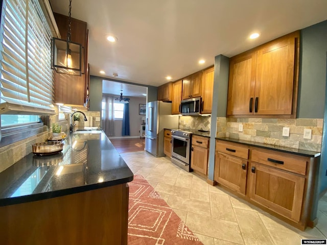 kitchen featuring kitchen peninsula, backsplash, appliances with stainless steel finishes, sink, and decorative light fixtures