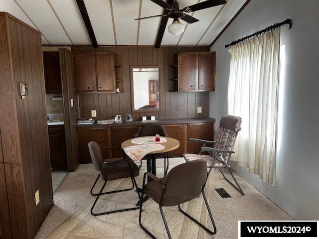 kitchen with wooden walls, lofted ceiling with beams, and ceiling fan