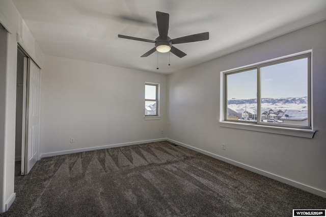 unfurnished bedroom with a closet, dark colored carpet, and ceiling fan