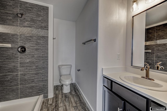 bathroom featuring a tile shower, vanity, toilet, and wood-type flooring