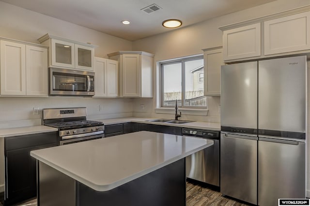 kitchen with appliances with stainless steel finishes, sink, hardwood / wood-style flooring, white cabinets, and a center island