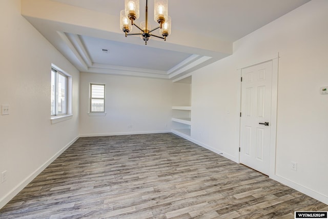 empty room with hardwood / wood-style flooring, a chandelier, and a tray ceiling