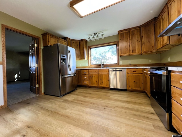 kitchen featuring stainless steel appliances, light hardwood / wood-style floors, wall chimney range hood, and sink