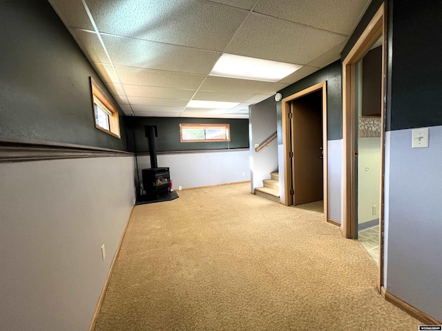 basement featuring a wealth of natural light, a paneled ceiling, carpet flooring, and a wood stove