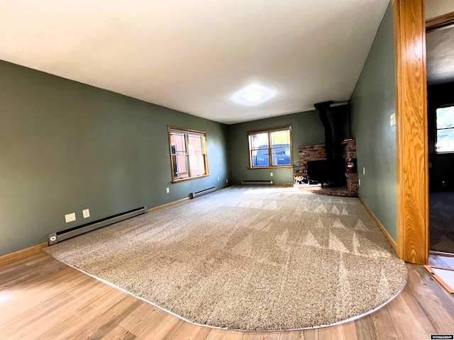 unfurnished living room featuring a wood stove, hardwood / wood-style floors, and a baseboard radiator