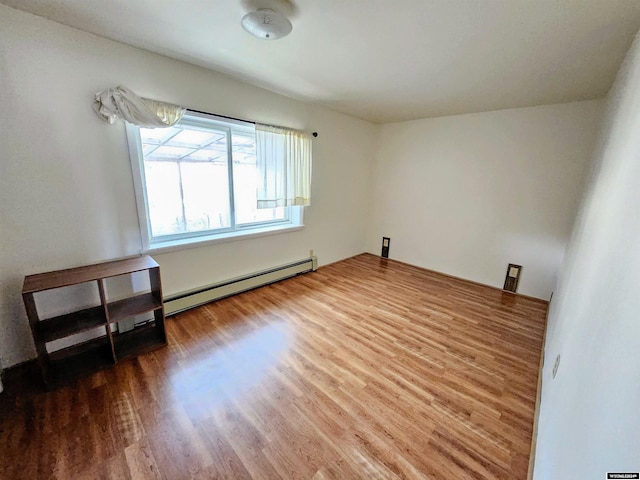 empty room with wood-type flooring and a baseboard heating unit