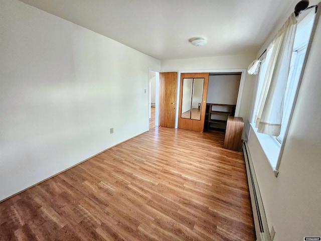 interior space with multiple windows, light wood-type flooring, a closet, and baseboard heating