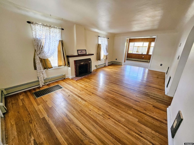 unfurnished living room with a baseboard heating unit, hardwood / wood-style floors, and a brick fireplace