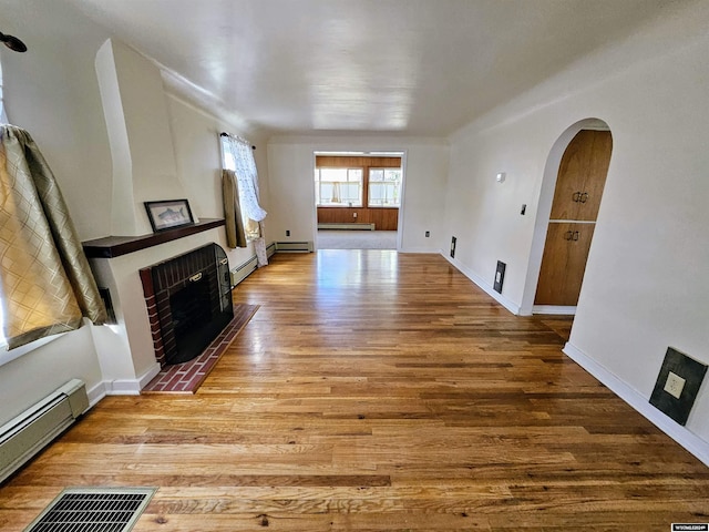 living room with light hardwood / wood-style floors, baseboard heating, and a brick fireplace