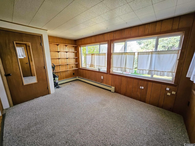 carpeted spare room with wooden walls and a baseboard heating unit