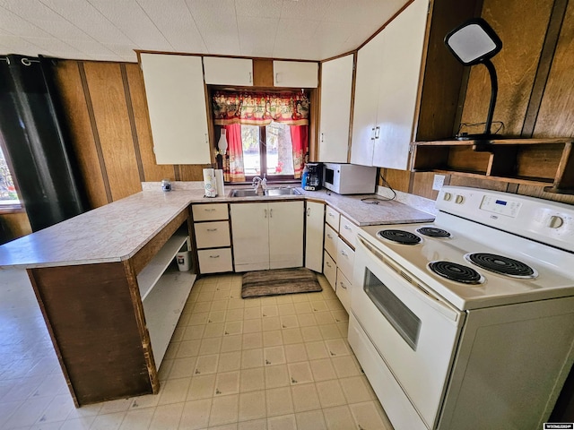 kitchen with white appliances, sink, wooden walls, white cabinetry, and kitchen peninsula