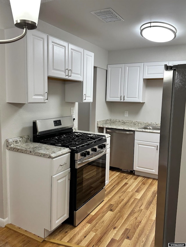 kitchen featuring stainless steel appliances, light stone counters, sink, white cabinetry, and light hardwood / wood-style flooring