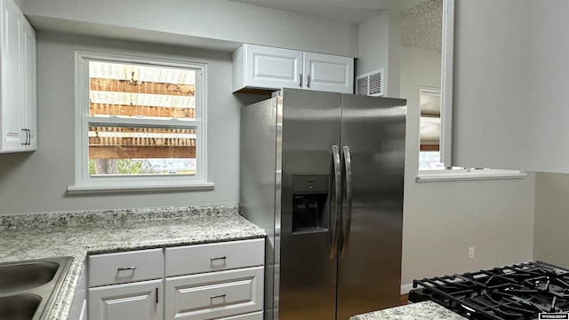 kitchen featuring white cabinets, stainless steel refrigerator with ice dispenser, and light stone counters