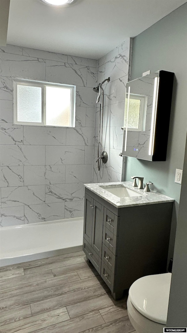 bathroom featuring tiled shower, hardwood / wood-style floors, vanity, and toilet