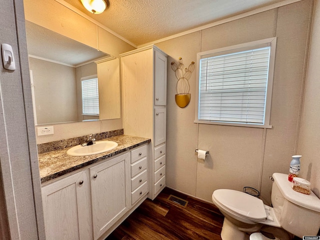 bathroom featuring wood-type flooring, toilet, a textured ceiling, ornamental molding, and vanity