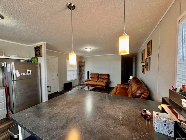 kitchen with hanging light fixtures, a textured ceiling, stainless steel refrigerator, and crown molding